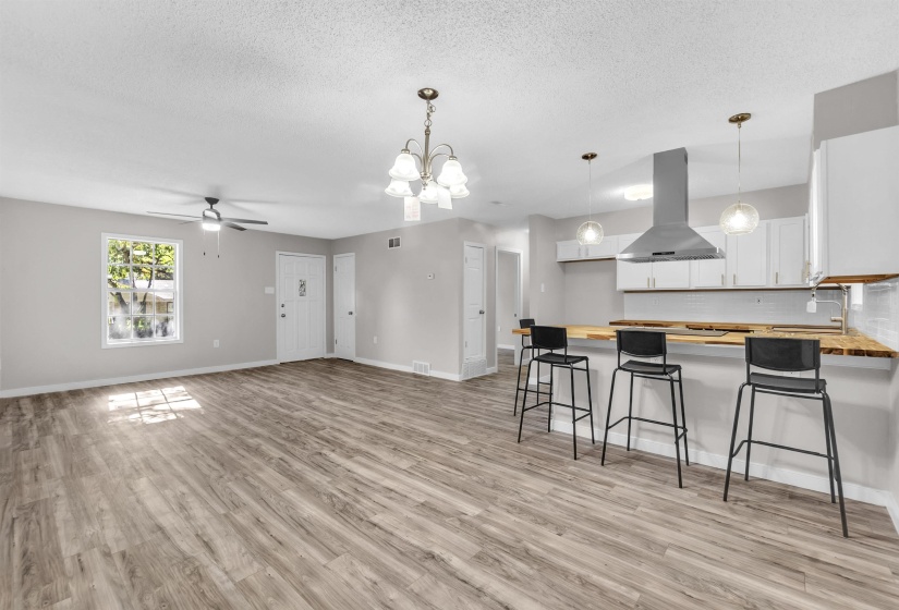Kitchen featuring a peninsula, butcher block counters, suspended lighting, a kitchen bar, and exhaust hood