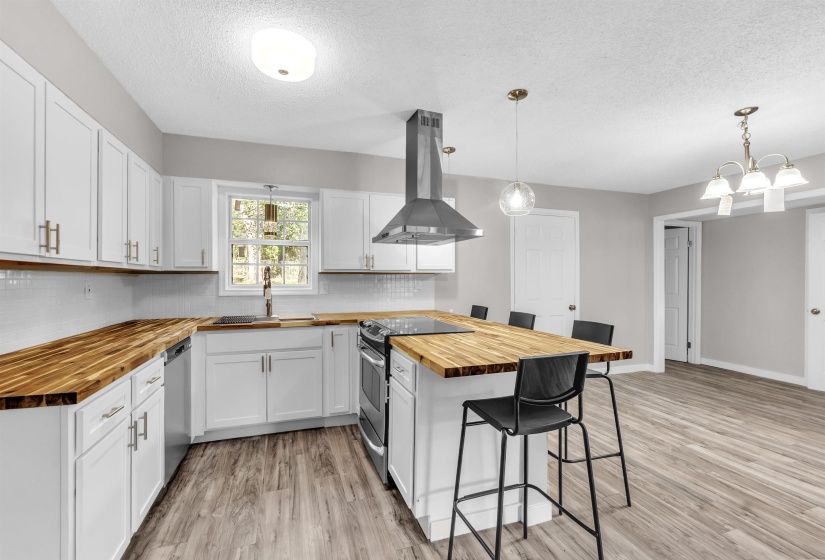 Kitchen with butcher block countertops, a breakfast bar, a peninsula, stainless steel appliances, and island range hood