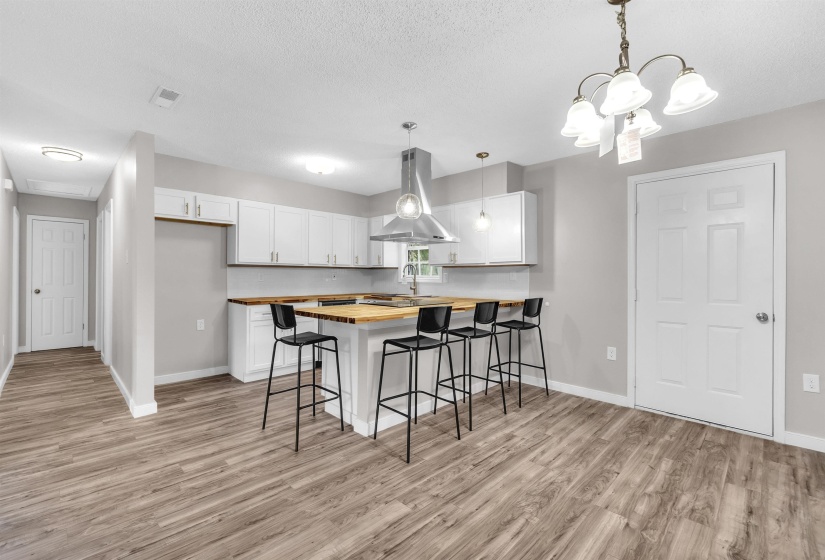 Kitchen with a breakfast bar area, wood counters, a peninsula, island exhaust hood, and white cabinetry