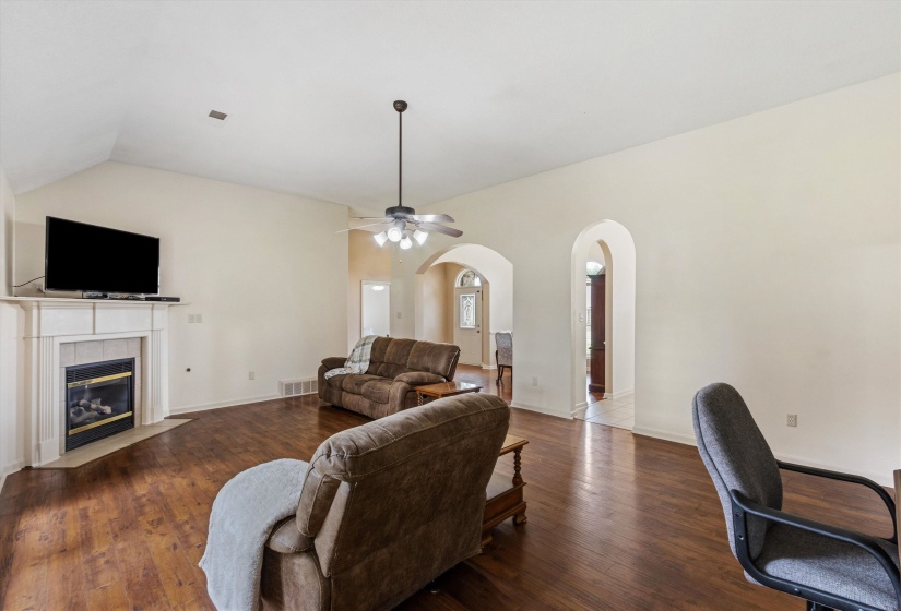 Living area featuring wood-finish flooring, a white mantel fireplace, a vaulted ceiling, and arched doorways