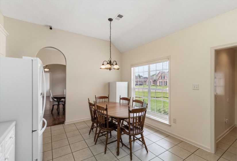Kitchen eating area featuring tile flooring, vaulted ceiling, and a large window with horizontal blinds
