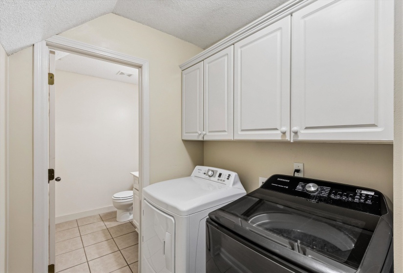 Utility area featuring white upper cabinetry, tiled flooring, and an adjacent room with a toilet and vanity