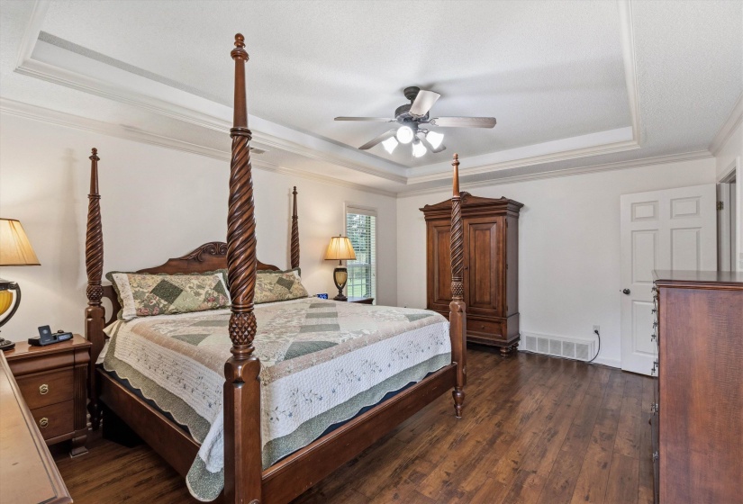 Spacious bedroom featuring rich wood-finish flooring, a tray ceiling, and crown molding