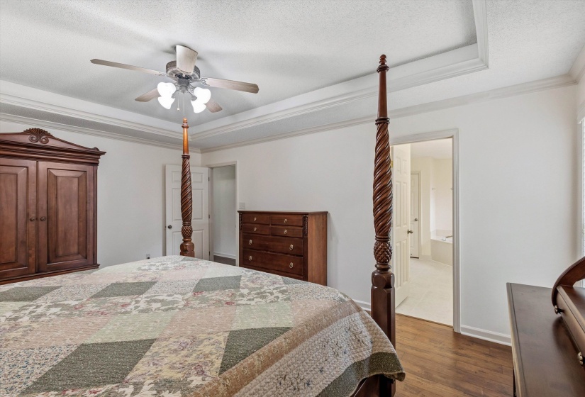 Bedroom featuring wood-finish flooring, a tray ceiling with crown molding, and a ceiling fan with integrated lighting