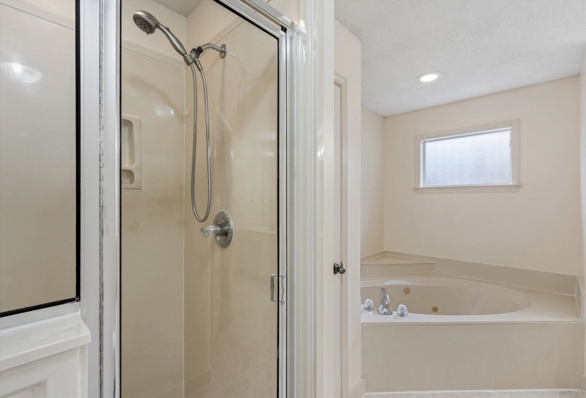 Enclosed glass shower with chrome fixtures and an integrated corner jetted tub