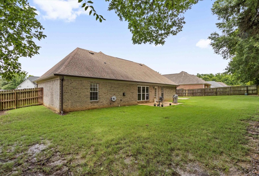 Brick exterior with a gabled roofline, featuring an expansive green lawn and wood privacy fencing