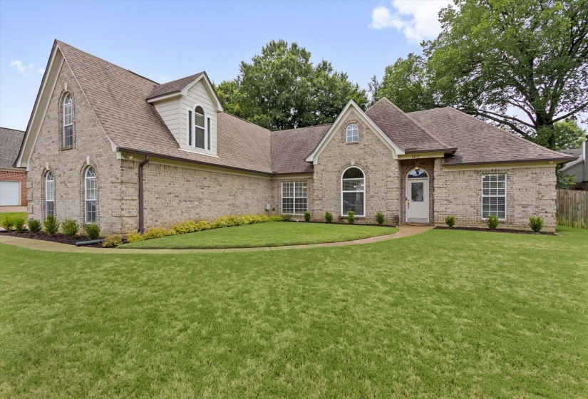 Traditional brick exterior featuring an arched entry, multiple gables, and a mature treeline backdrop
