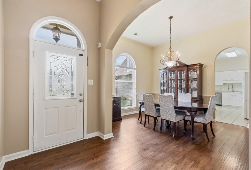Entry foyer featuring a decorative glass paneled door with an arched transom, wood-finish flooring, and arched doorways opening to a dining area and kitchen