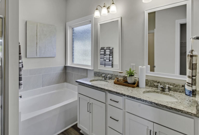 Full bath with double vanity, a garden tub, and dark wood finished floors