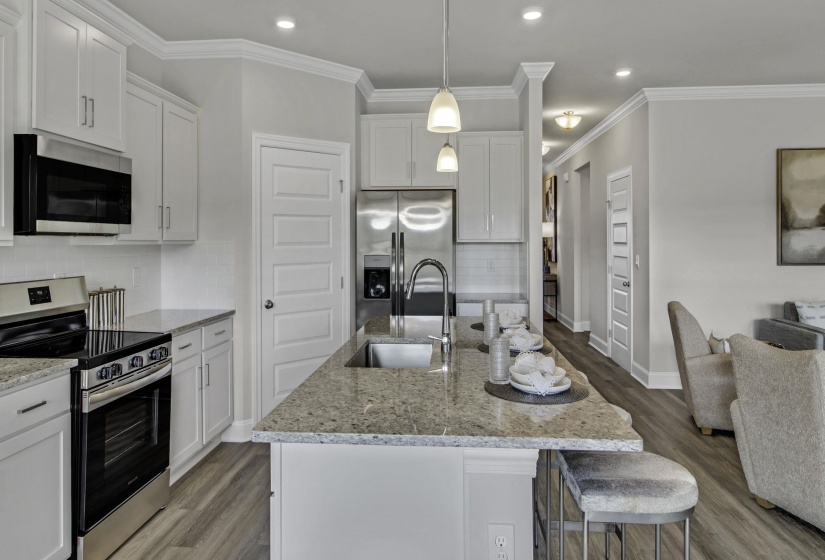 Kitchen with stainless steel appliances, white cabinets, light stone countertops, light wood-style floors, and ornamental molding
