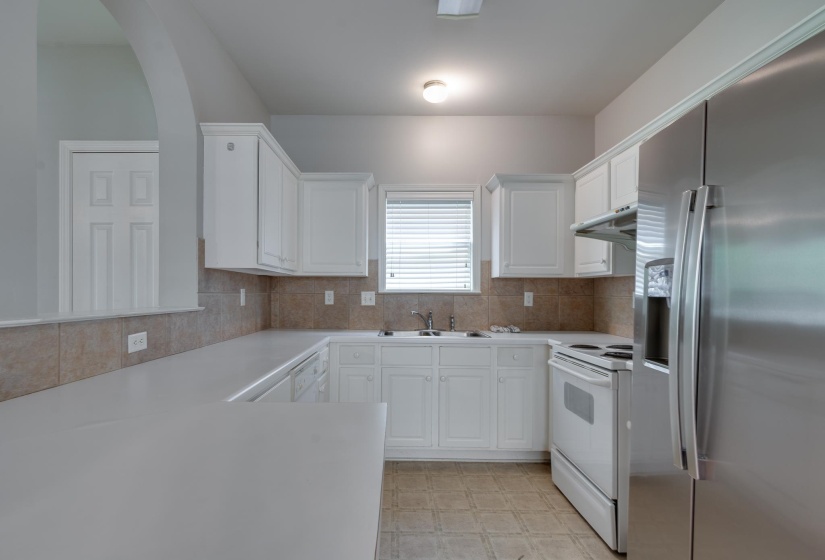 Kitchen featuring white cabinetry, light-toned countertops, a stainless steel refrigerator, white range, and a tile backsplash