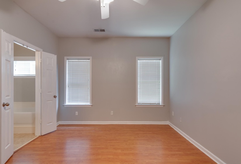 Spacious room featuring light wood-finish flooring, two windows with blinds, and a ceiling fan