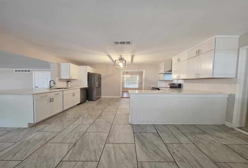 Open-concept kitchen featuring wood-finish tile flooring, white cabinetry, integrated stainless steel appliances, and a central island with a breakfast bar