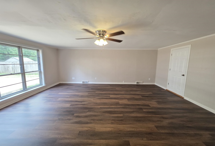Spacious interior featuring wood-finish flooring, a large multi-pane window, neutral wall tones, and a ceiling fan with integrated lighting