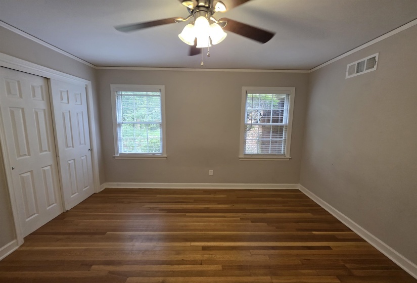 Room featuring wood-finish flooring, two windows with blinds, a ceiling fan with integrated lighting, and a closet with bifold doors