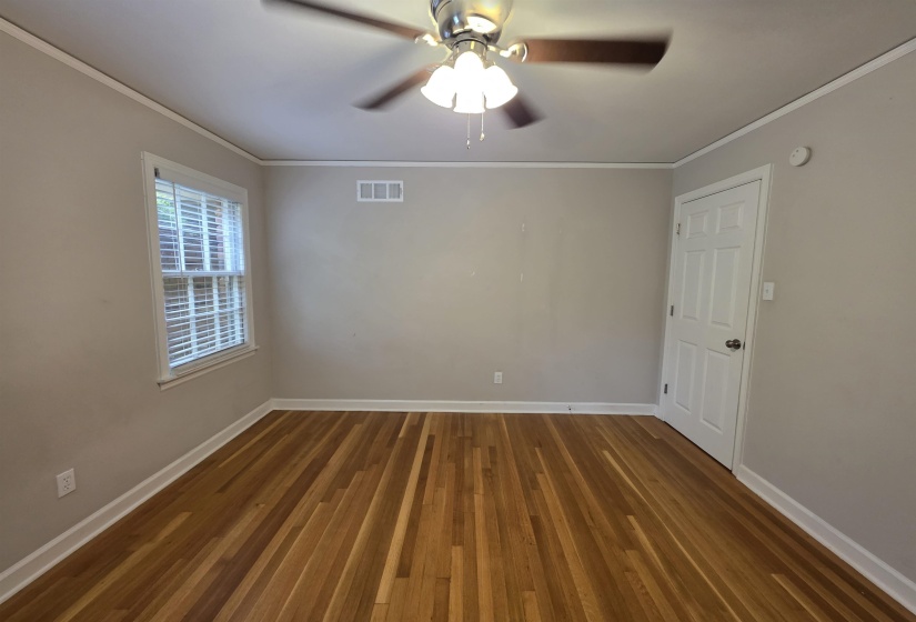 Spacious room featuring wood-finish flooring, a ceiling fan with light fixture, white trim, and a multi-pane window with blinds