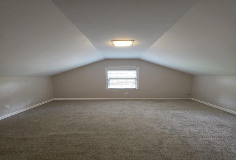 Carpeted room featuring a single window with blinds, sloped ceilings, and a flush-mount ceiling light fixture