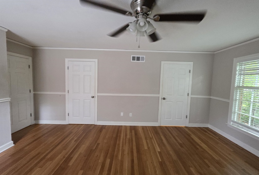 Room featuring wood-finish flooring, two white paneled doors, chair rail molding, a ceiling fan with integrated lighting, and a window with blinds