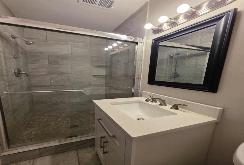 Contemporary bathroom featuring a glass-enclosed shower with gray tile surround and pebble-style flooring