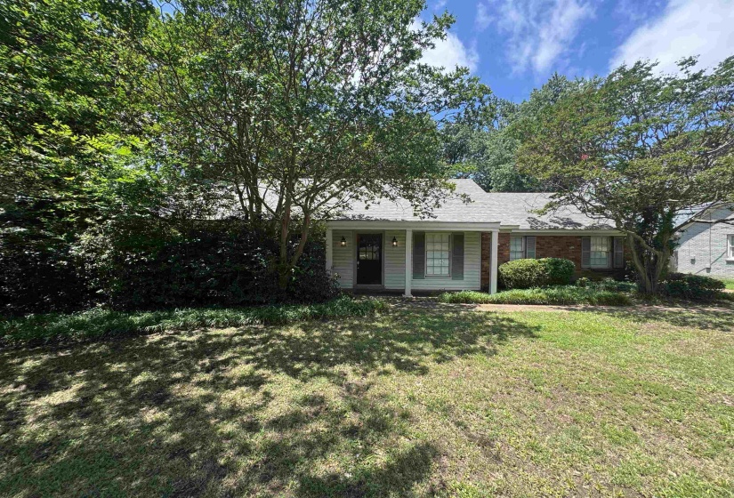 Traditional-style residence featuring a prominent front lawn, mature trees, and a covered entry porch