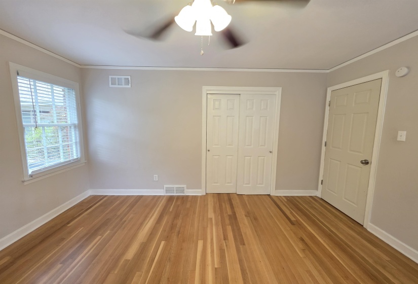 Hardwood flooring throughout, featuring a double-pane window, white baseboards, and crown molding