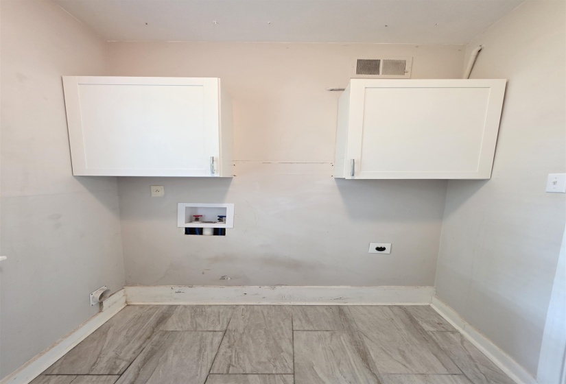 Utility area featuring tile flooring, two wall-mounted white cabinetry units, and plumbing hookups