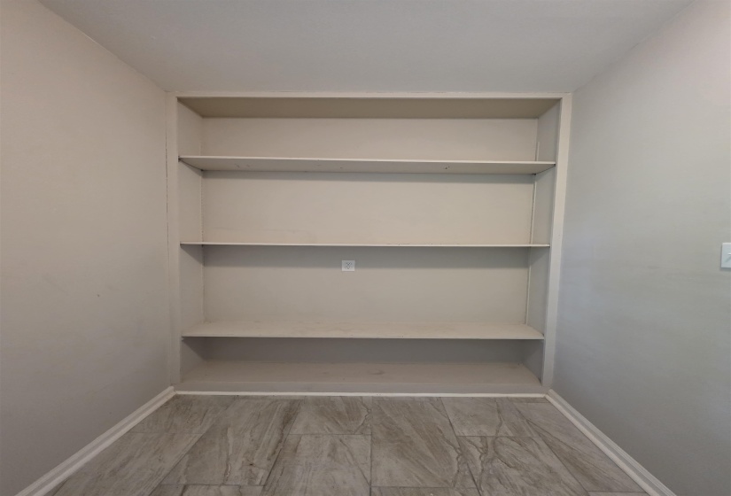 Built-in shelving unit with four levels of storage, set within an alcove with light gray walls and wood-finish flooring