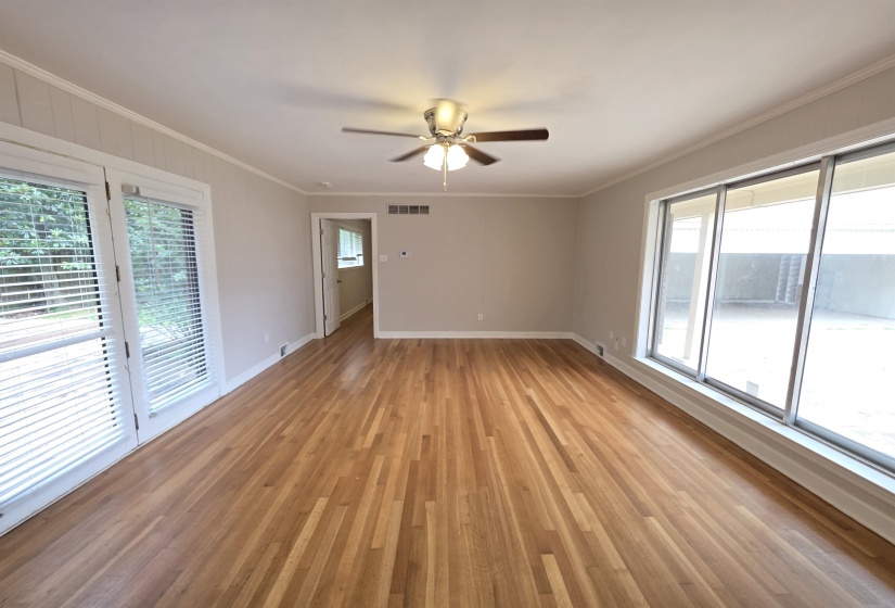 Spacious room featuring wood-finish flooring, a ceiling fan, and extensive natural light from glass paneled doors and a large sliding glass window