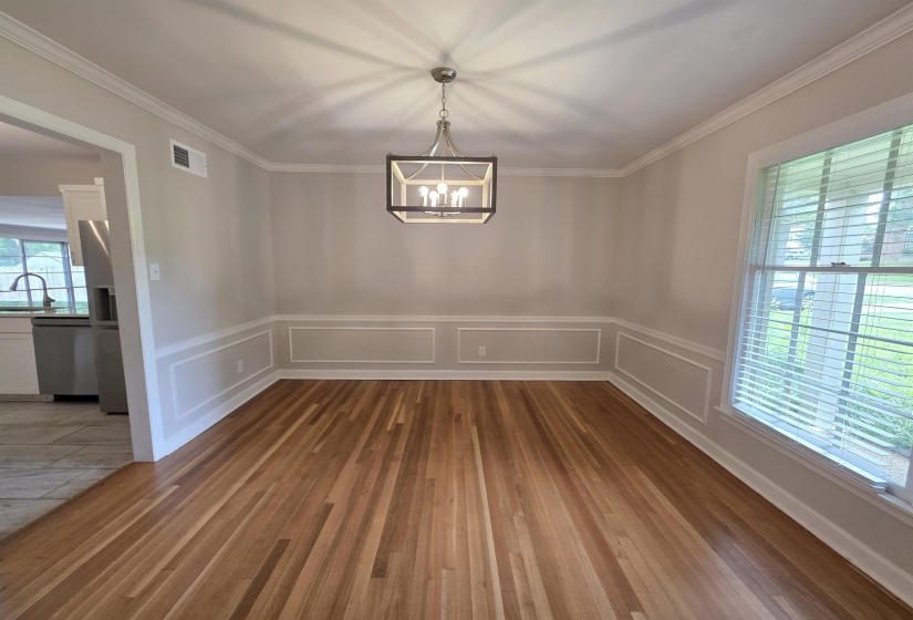 Formal dining space featuring wood-finish flooring, wainscoting, crown molding, and a contemporary chandelier