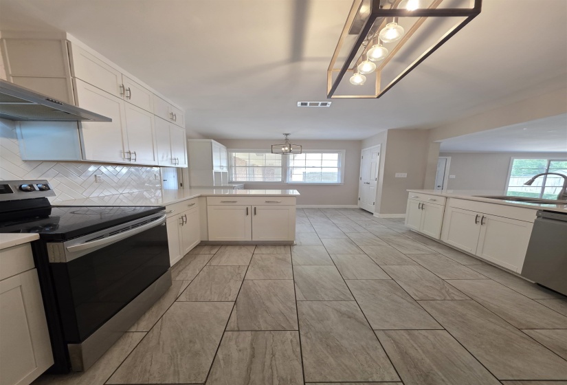 Modern kitchen featuring white shaker cabinetry, light-toned countertops, a herringbone tile backsplash, stainless steel appliances, and large format plank tile flooring