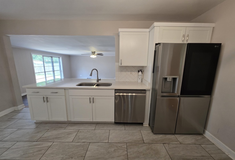 Kitchen featuring white shaker-style cabinetry, a stainless steel sink with a gooseneck faucet, light-toned countertops, and a subway tile backsplash