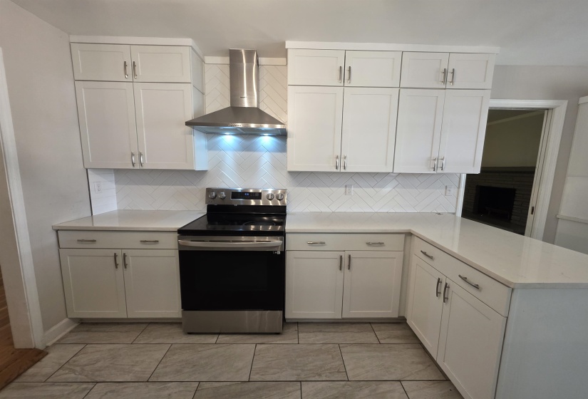 Modern kitchen featuring white shaker cabinetry, light-toned countertops, a herringbone tile backsplash, stainless steel appliances, and large format tile flooring