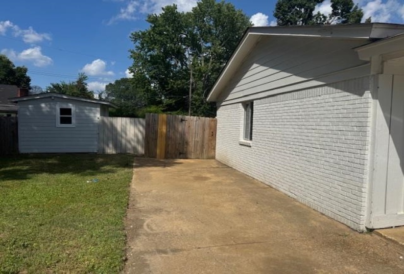 View of side of home with brick siding, a storage unit, and a patio area