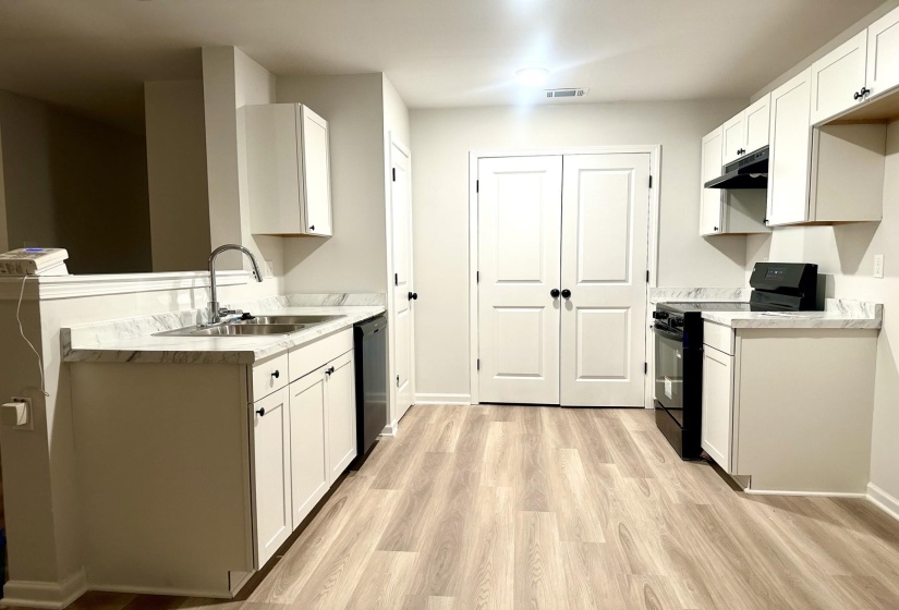 Contemporary kitchen featuring wood-finish flooring, white cabinetry with black hardware, stone-look countertops, and a double-basin stainless steel sink with a high-arch faucet