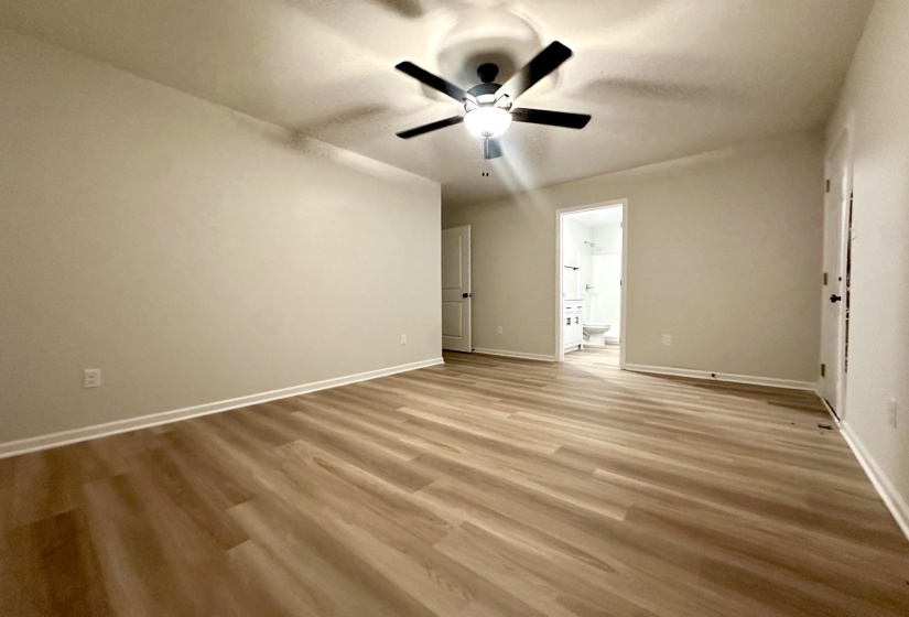 Spacious room featuring wood-finish flooring, light neutral wall tones, and a ceiling fan with integrated lighting
