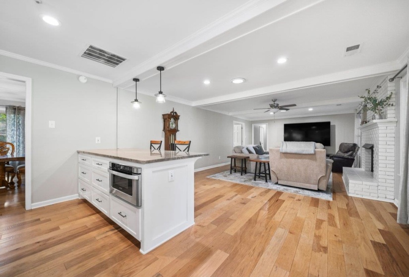 Open-concept living space featuring wood-finish flooring, a kitchen island with built-in stainless-steel microwave, pendant lighting