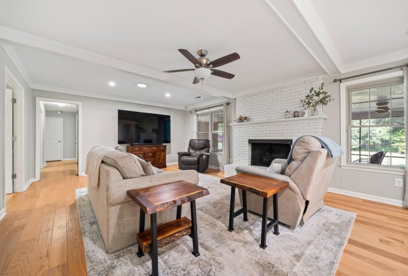 Den area featuring light wood-finish flooring, a white painted brick fireplace with a mantel, recessed lighting, and a ceiling fan