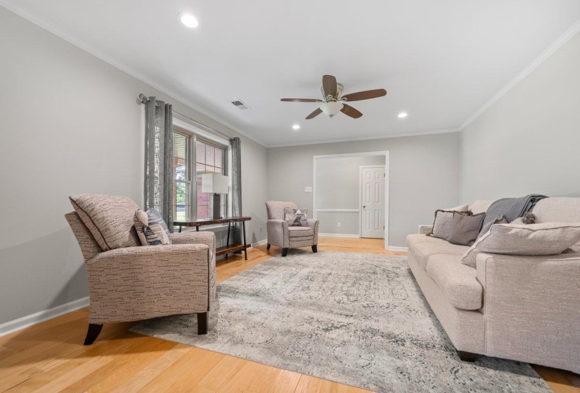 Brightly lit living area featuring hardwood flooring, recessed lighting, crown molding, a ceiling fan, and a large window.