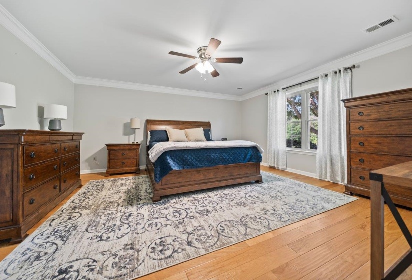 Spacious Large primary bedroom featuring wood-finish flooring, a ceiling fan with light fixture, large window, and crown molding