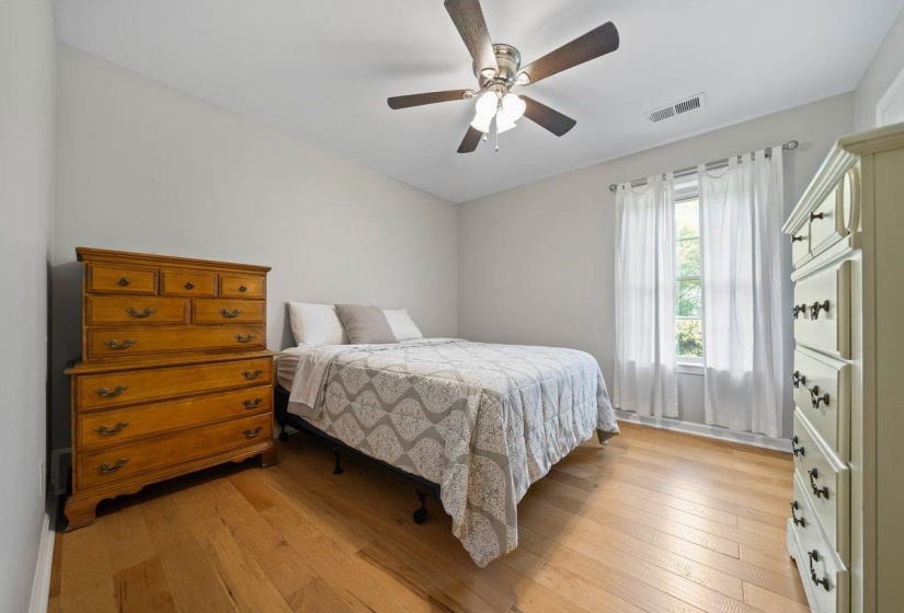 Light-filled room featuring wood-finish flooring, a ceiling fan, and a single window with white drapery panels