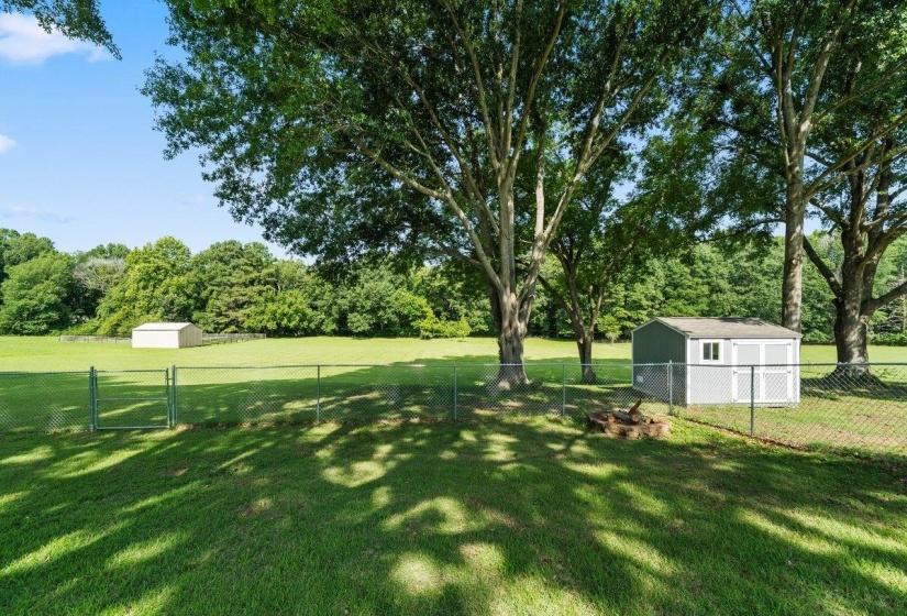 Expansive fenced backyard featuring mature shade trees, a fire pit area, and a storage shed