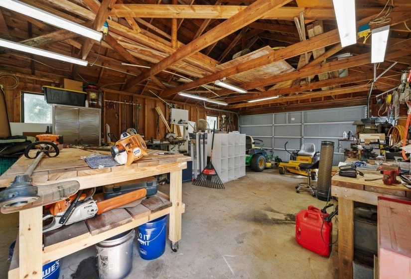 Spacious garage featuring exposed wood beam ceilings, concrete flooring, and a large roll-up door