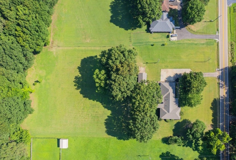 Expansive property featuring a single-story residence with a gray shingle roof, mature trees, and a paved driveway
