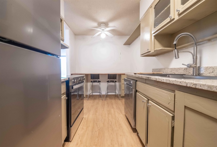 Kitchen featuring stainless steel appliances, wood-finish flooring, light-toned cabinetry, light-toned countertops, and a ceiling fan