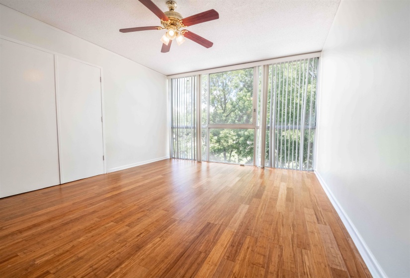 Bright terior featuring expansive windows with vertical blinds, wood-finish flooring, a ceiling fan, and white walls