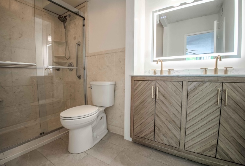 Contemporary bathroom featuring a double vanity with textured wood-finish cabinetry, a large illuminated mirror, and a glass-enclosed shower
