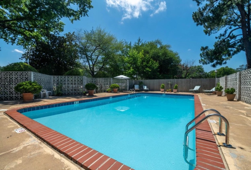 Outdoor swimming pool with a concrete surround, brick coping, and steel handrails