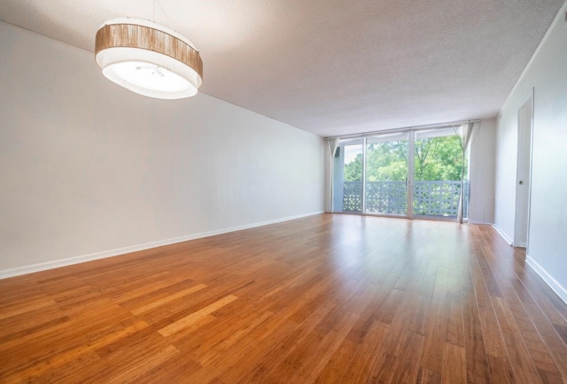 Spacious room featuring wood-finish flooring, a contemporary oval chandelier, and a large sliding glass door opening to an outdoor balcony