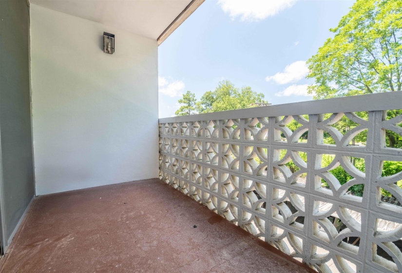 Balcony featuring a decorative block privacy screen, wall-mounted lighting fixture, and a durable floor surface