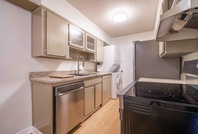 Kitchen featuring light-toned cabinetry, granite-finish countertops, stainless steel dishwasher, and a black flat-top electric range